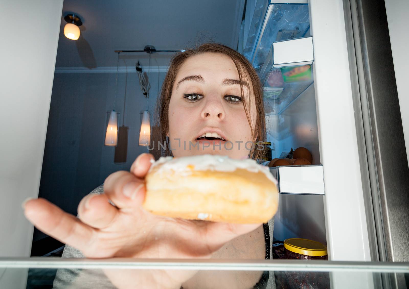 Wide angle portrait of woman taking donut from fridge