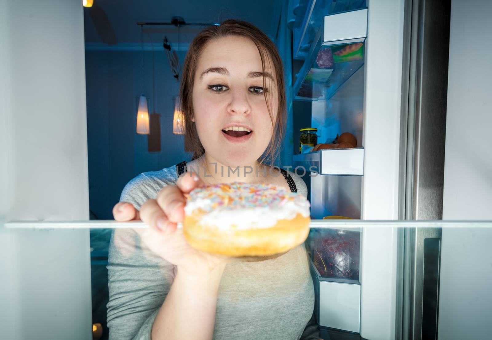 Closeup portrait of young woman taking donut out of fridge at night