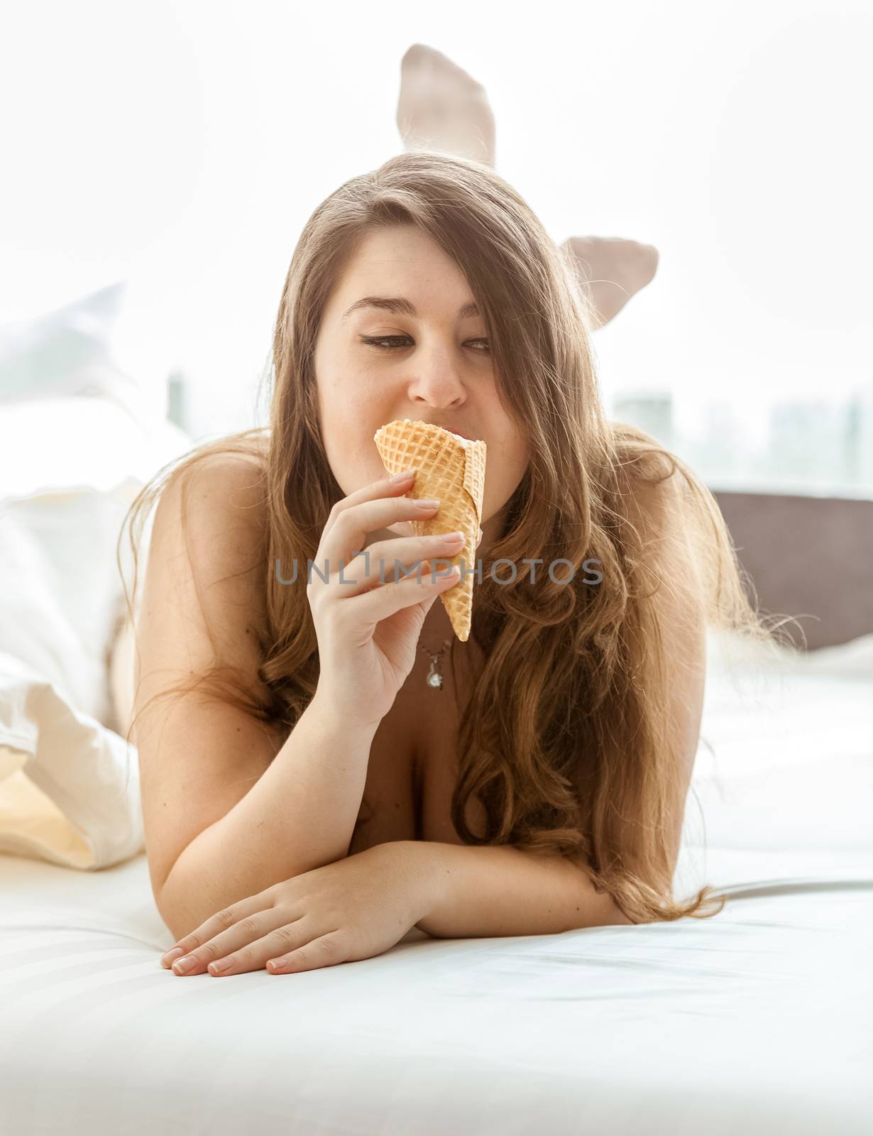 Brunette woman lying in bed and licking ice cream