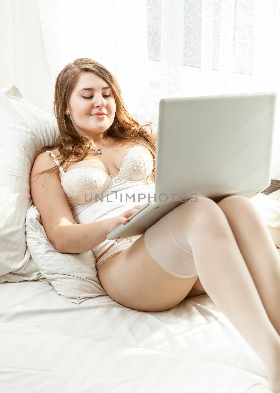 Beautiful woman in lingerie using laptop in bed