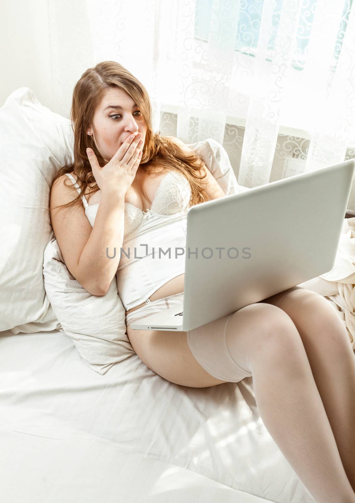 Beautiful amazed woman having video conference while lying in bed