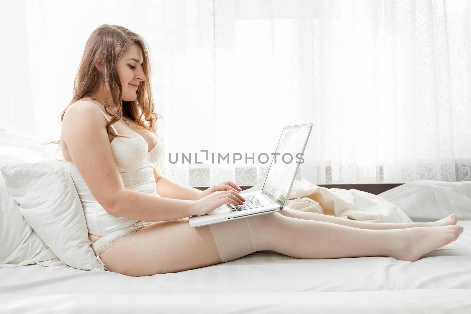 Beautiful brunette woman sitting on bed and using laptop