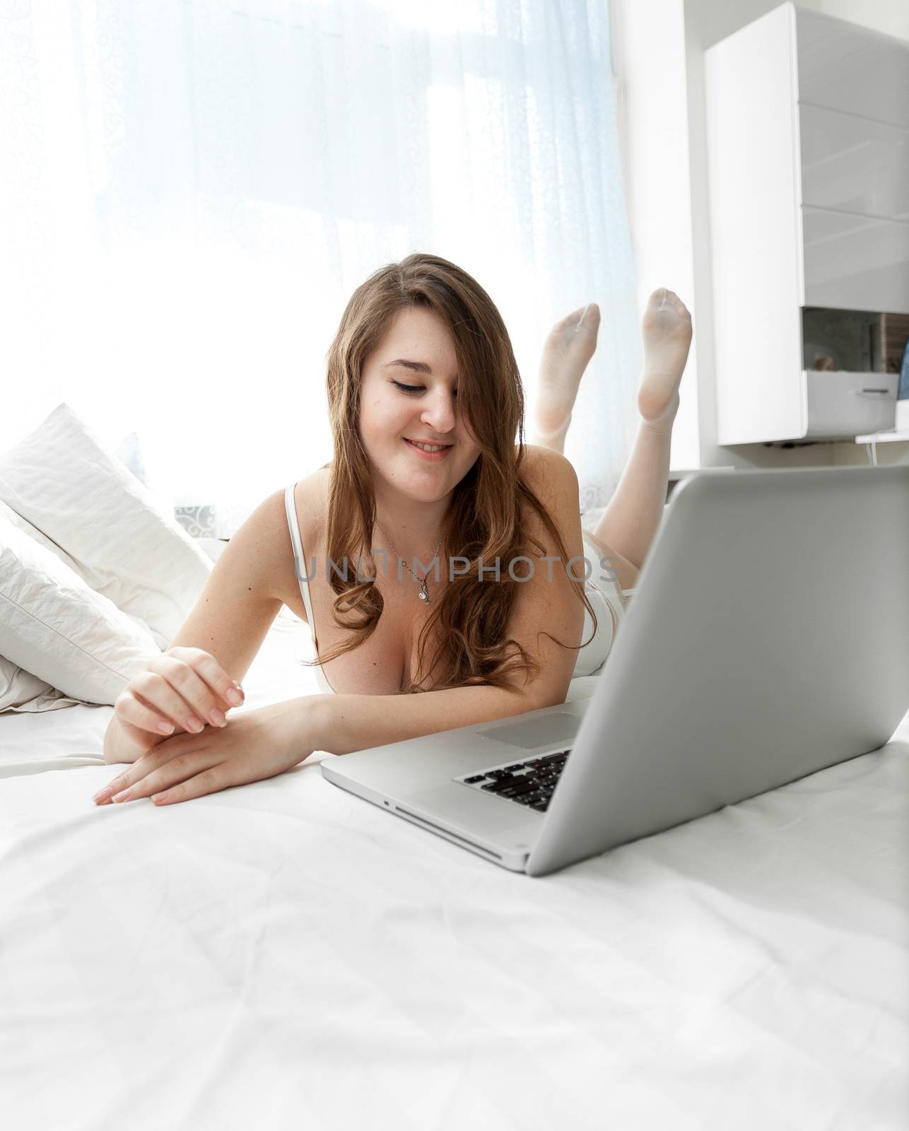 Beautiful brunette woman using laptop in bed at morning