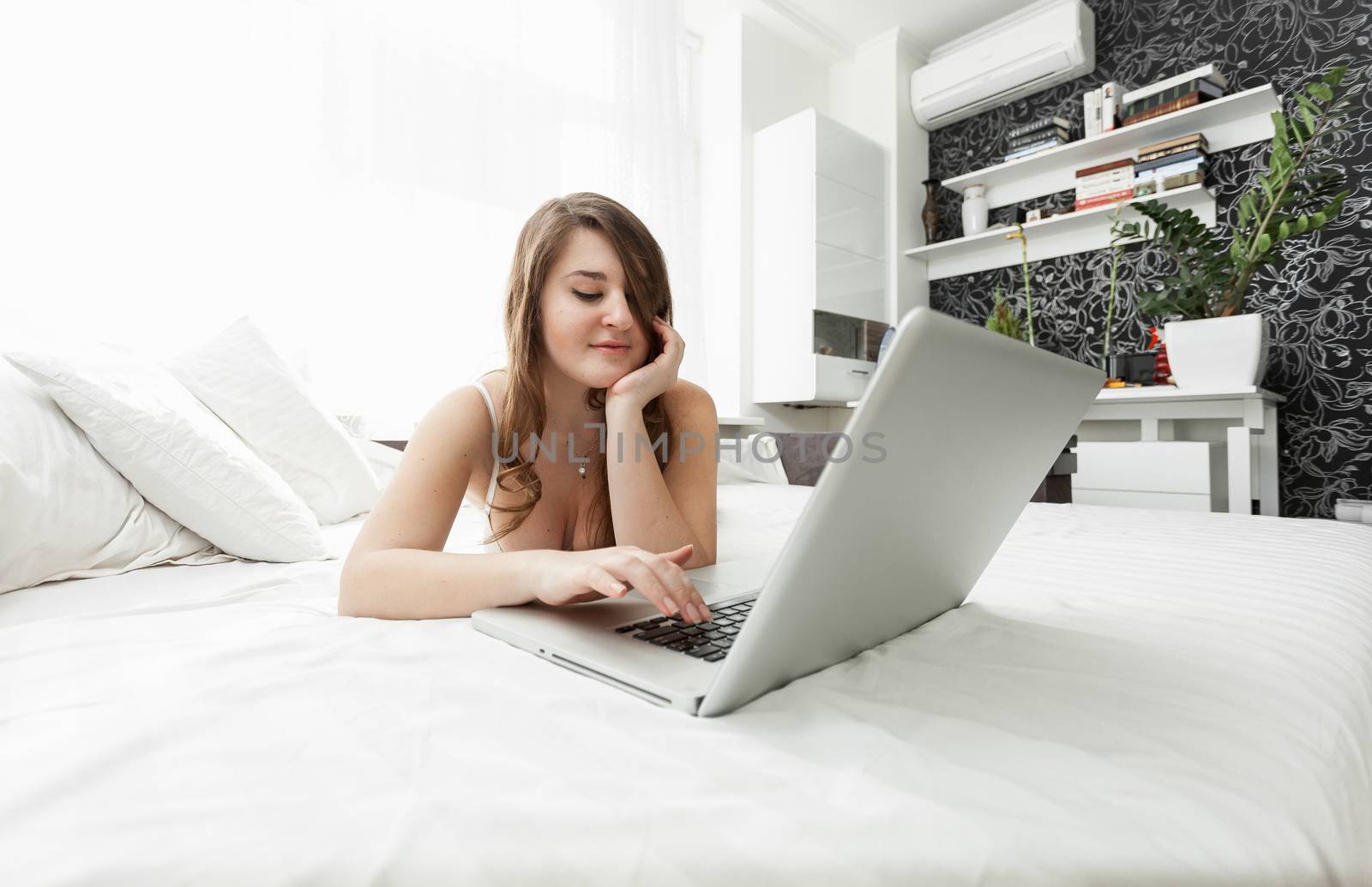 Beautiful woman working at home with laptop in bed