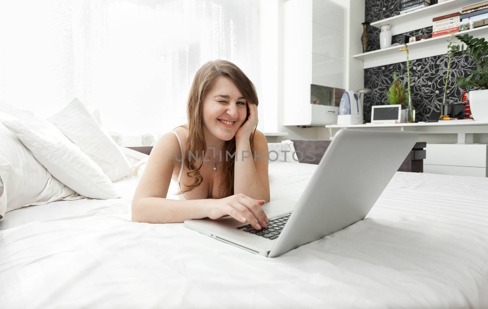smiling woman working on laptop in bed by Kryzhov