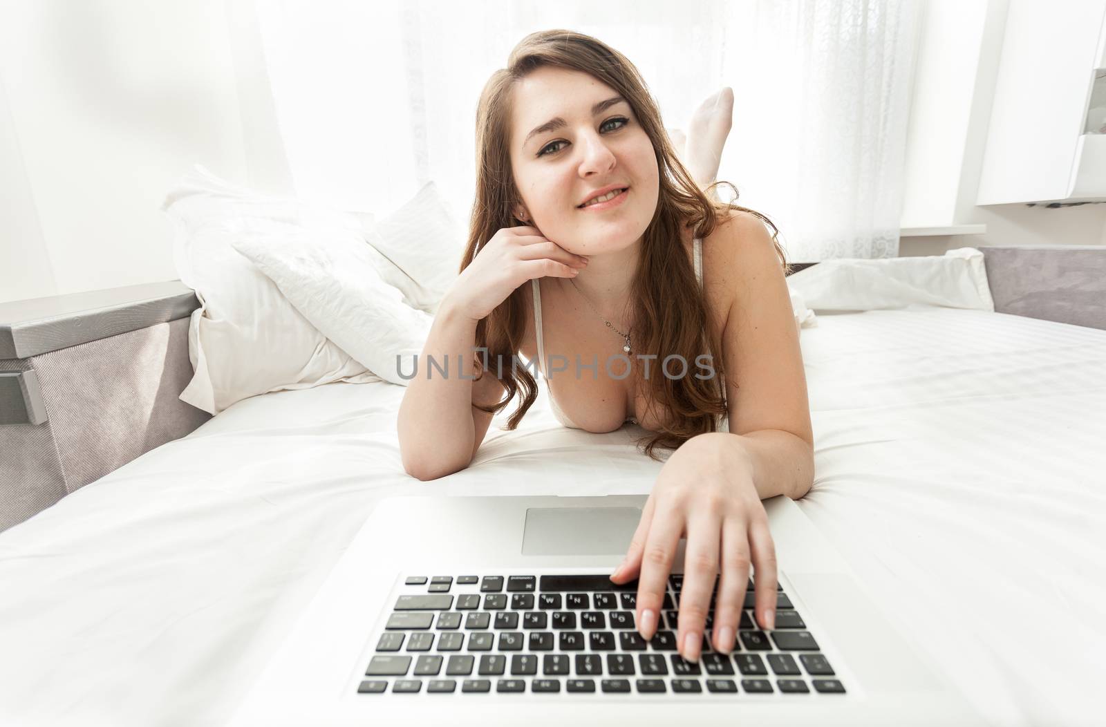 brunette woman using laptop keyboard in bed by Kryzhov