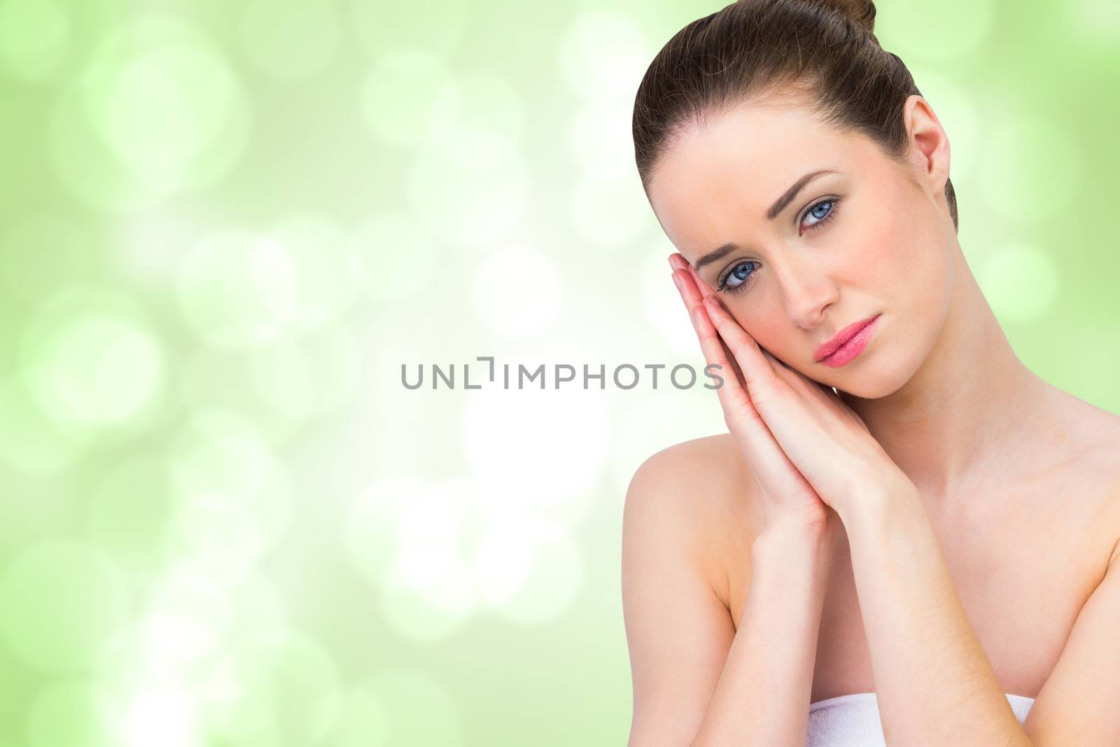 Beautiful brunette with hands at face against green abstract light spot design