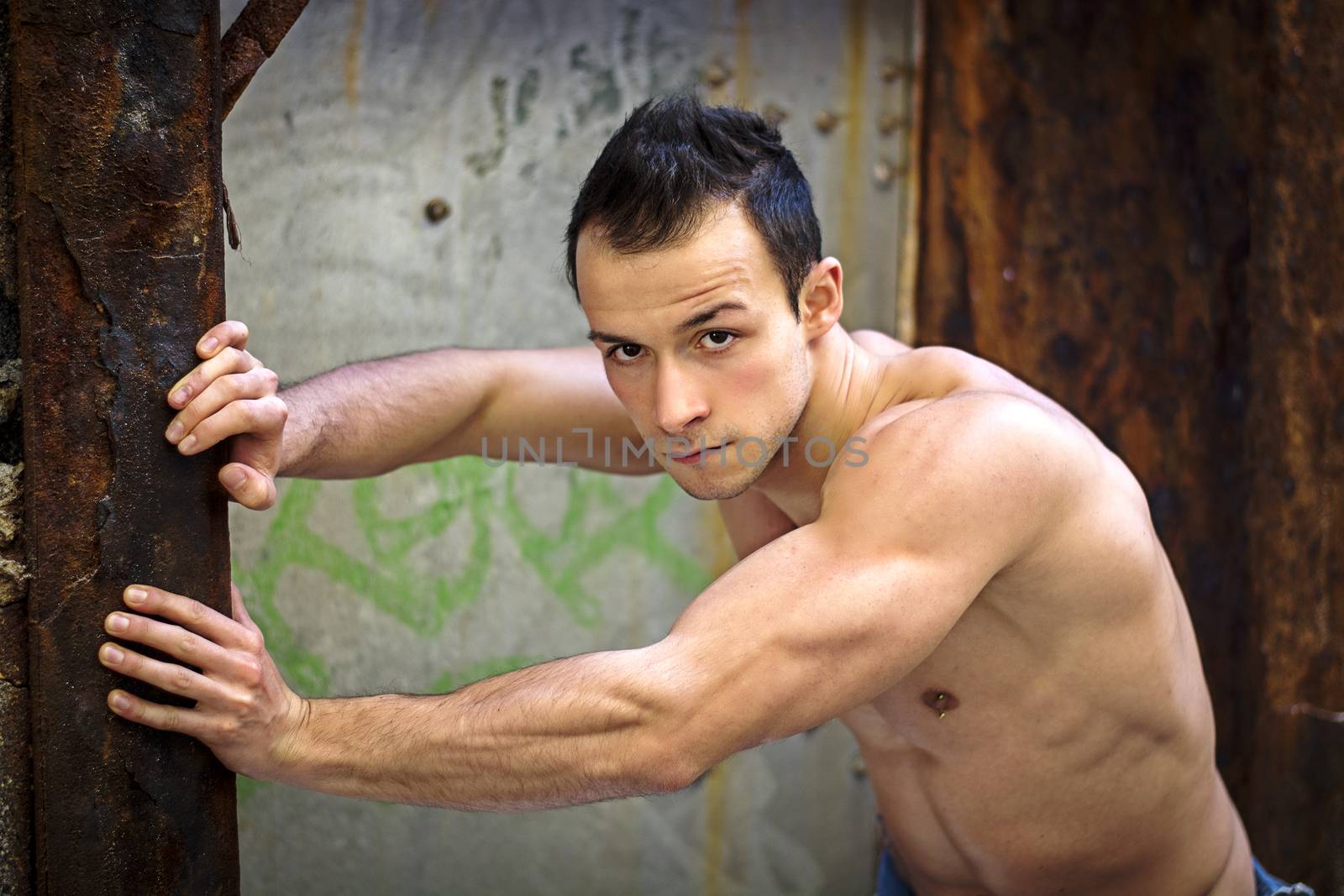 Muscular young man standing, leaning against rusty metal structure by artofphoto