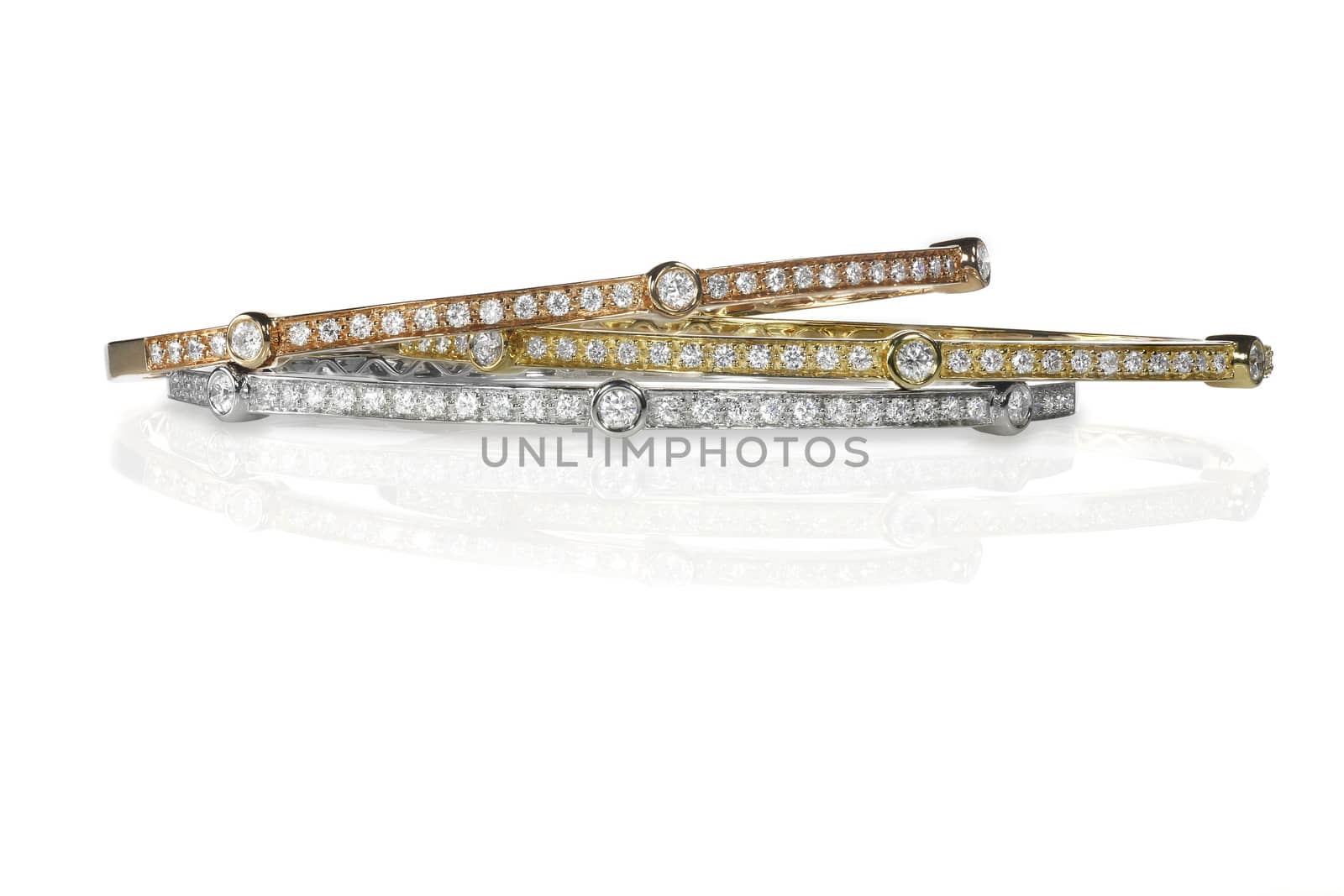 Set of three colored gold and diamond bracelets stacked isolated on white with a reflection