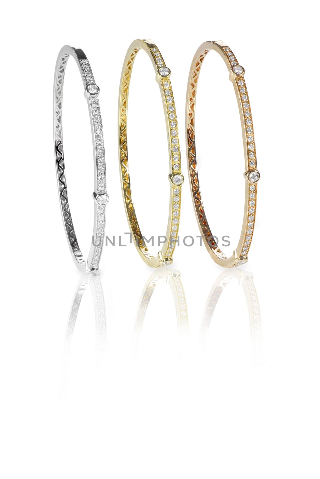 Set of three colored gold diamond bangle bracelets standing upright isolated on white with a reflection