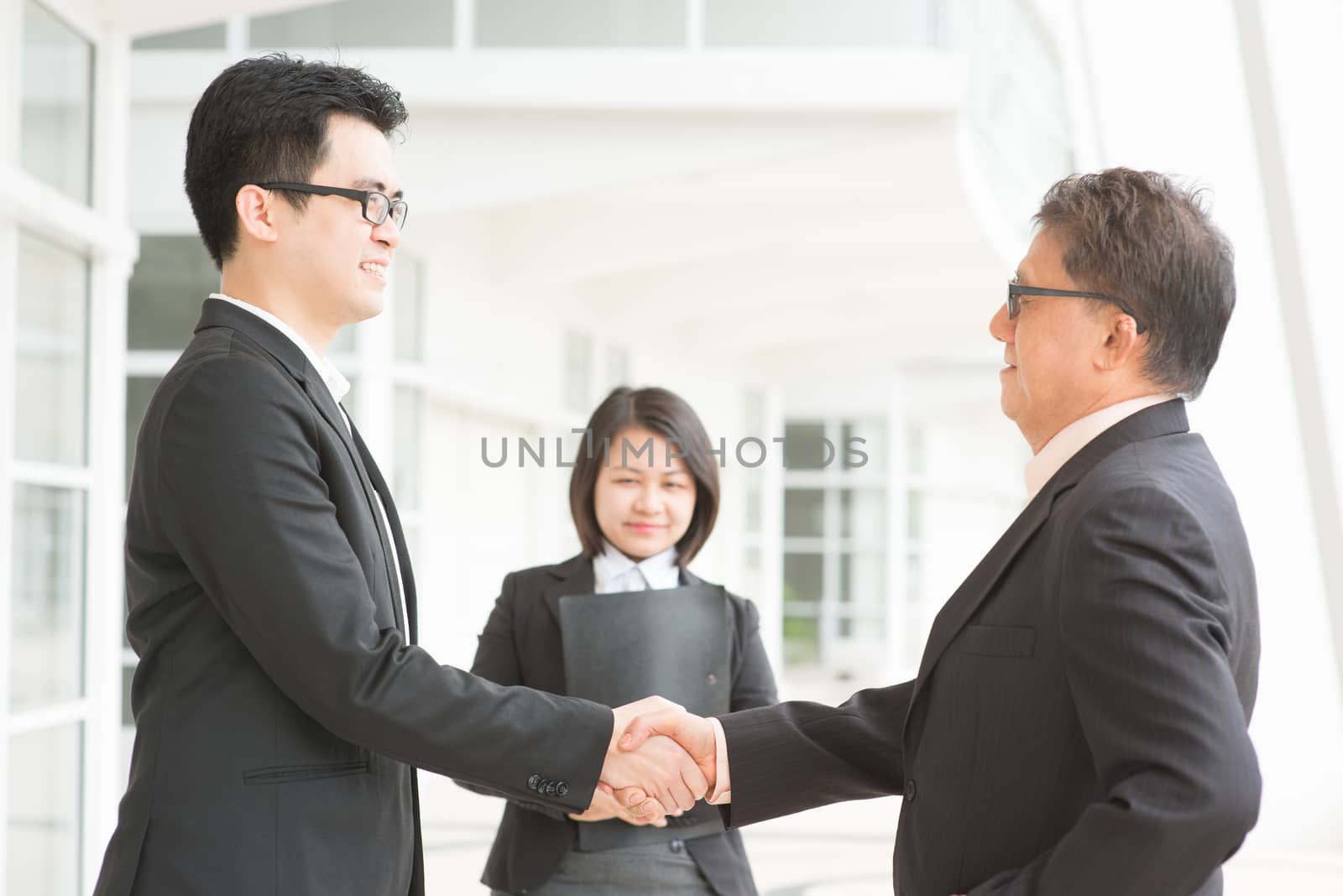 Business deal, Asian businessmen handshaking. Senior CEO hand shake with young executive. Modern  office building architecture background.