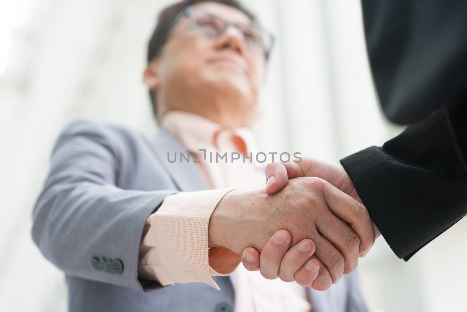 Business greeting, Asian businessmen handshaking. Chinese CEO boss. Focus on hands. Modern  office building architecture background.