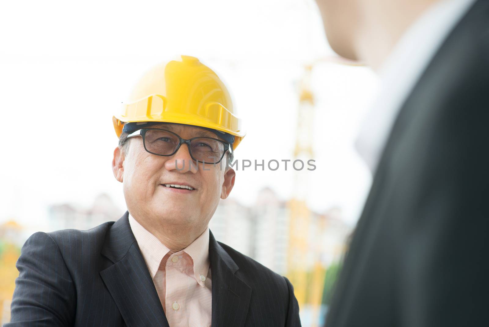 Senior male architect inspecting site with team member, construction site as background.