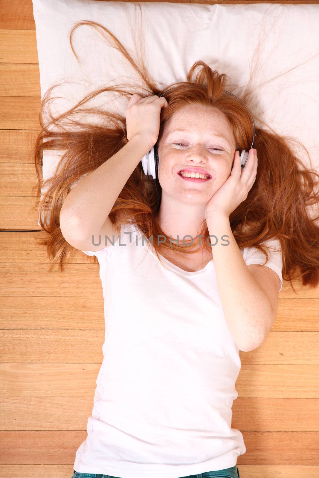 A young redhead girl lying on the floor while listening music.
