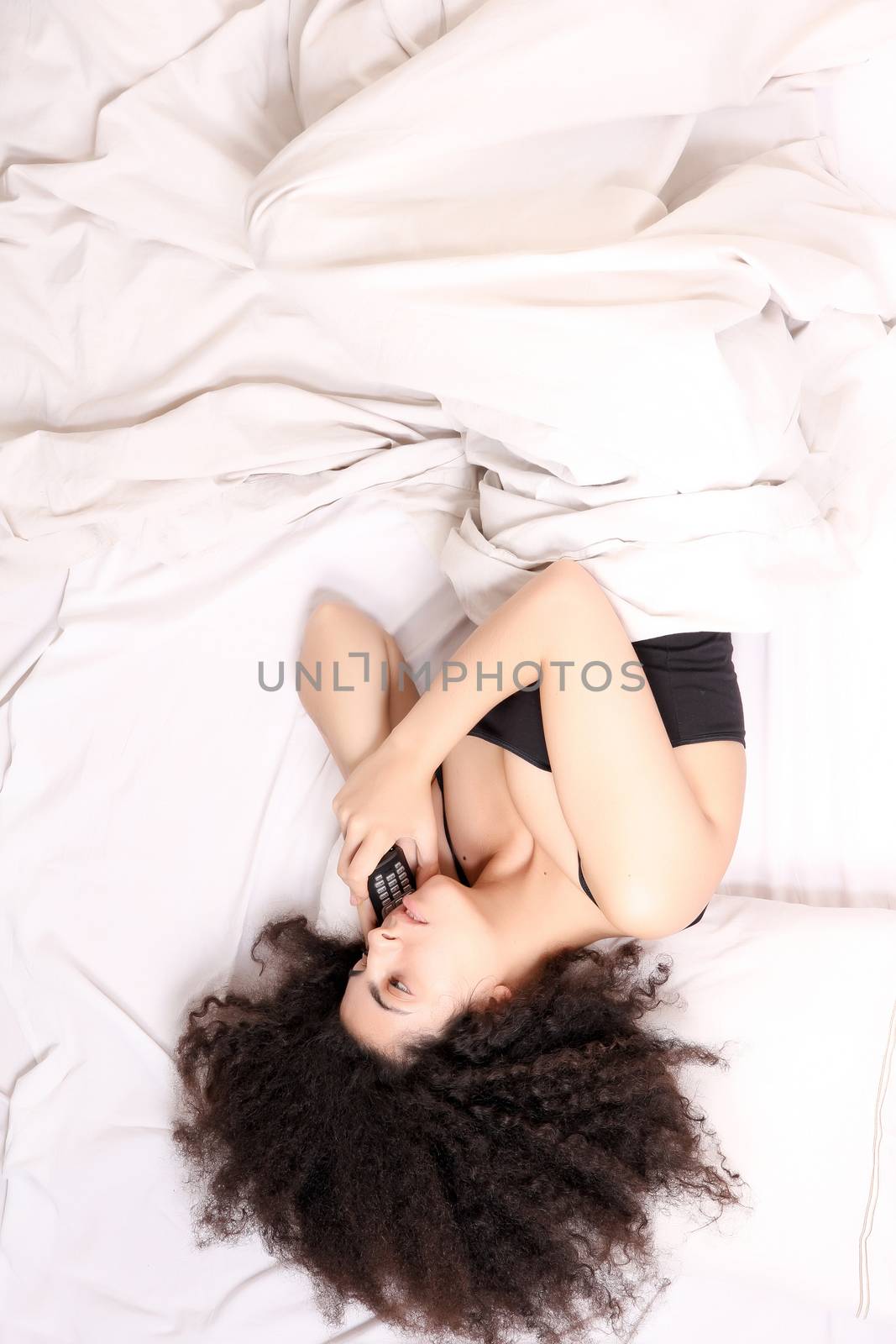 A young latin woman talking on the phone while lying in bed.