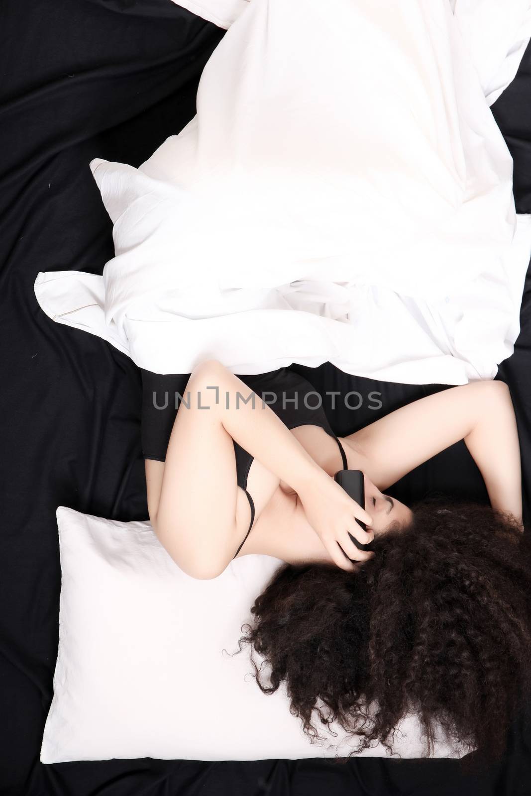 A young latin woman talking on the phone while lying in bed.