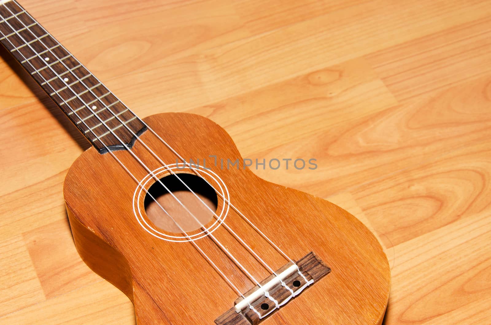The ukulele is placed on a vintage wooden floor.