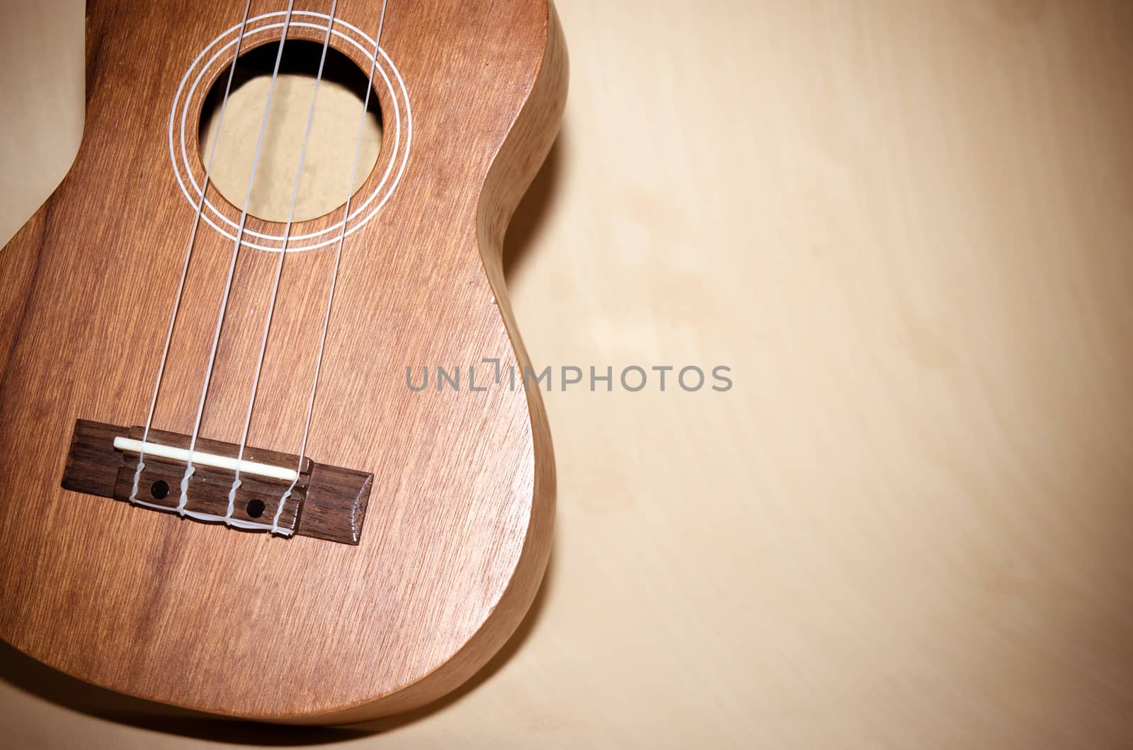 The ukulele is placed on a vintage wooden floor.