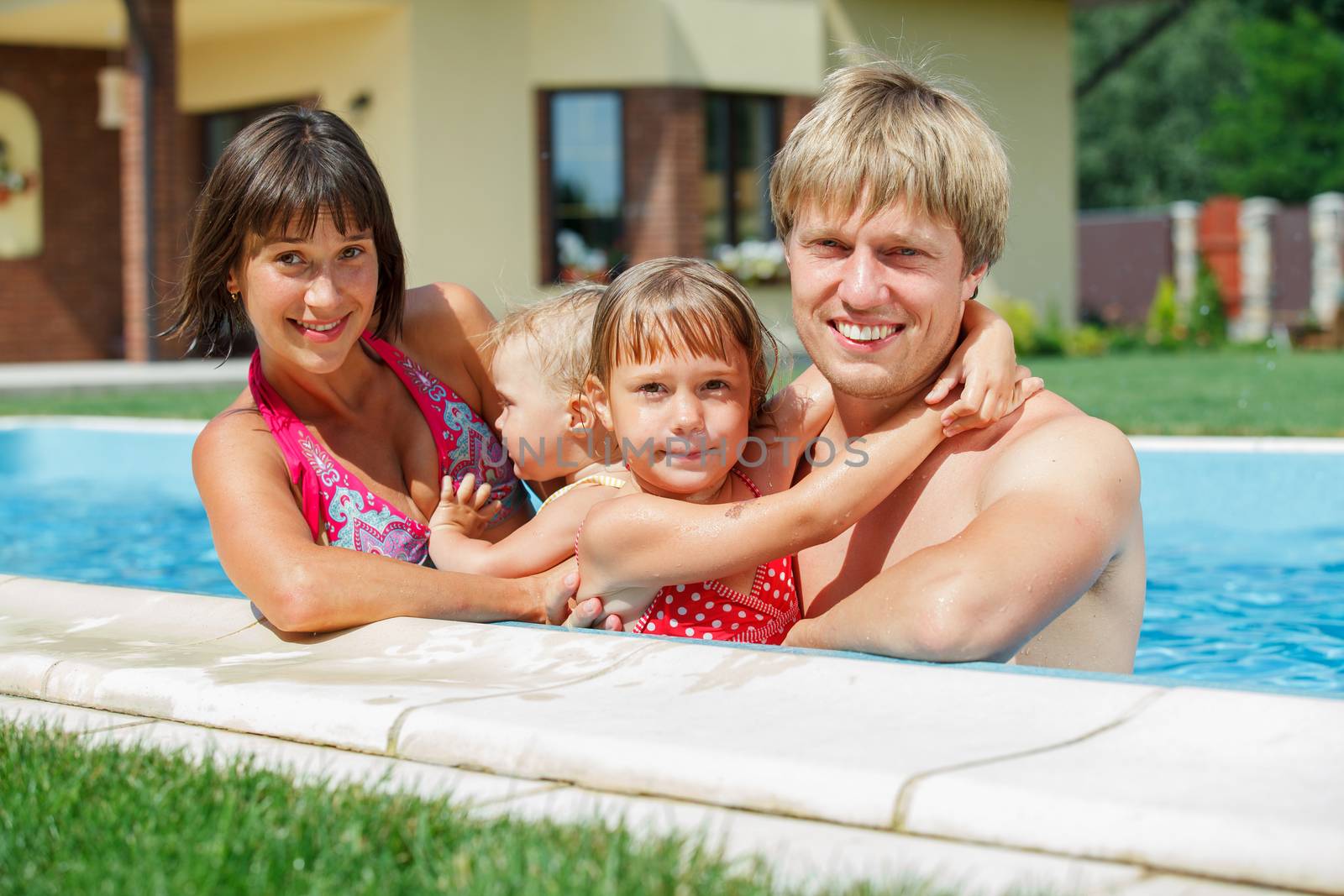 Summer vacations concept. Happy family with two kids playing in blue water of swimming pool.