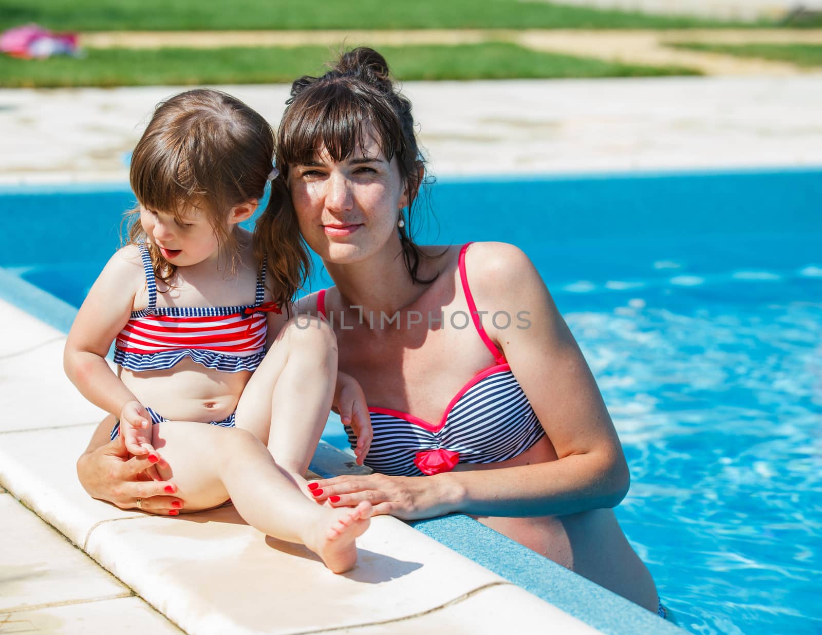 Summer vacations concept. Happy mother and daughter playing in blue water of swimming pool.