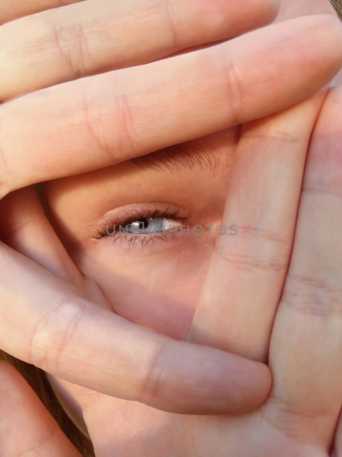 Fingers covering a blue eye which is squinting