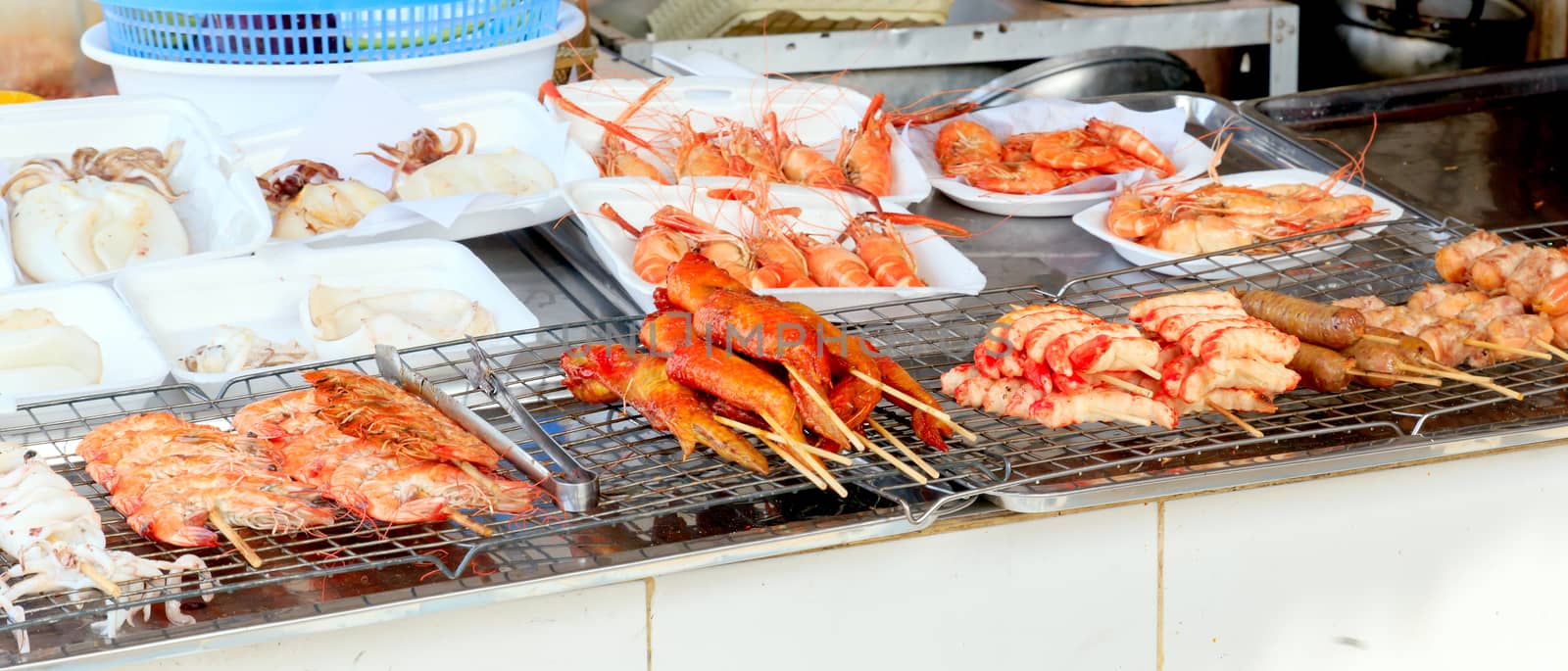Shrimp, squid, meatball and chicken skewers on the grill for sale.