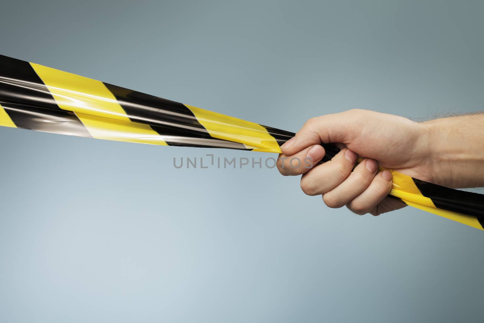 Man holding a yellow and black plastic barrier tape in his hand.