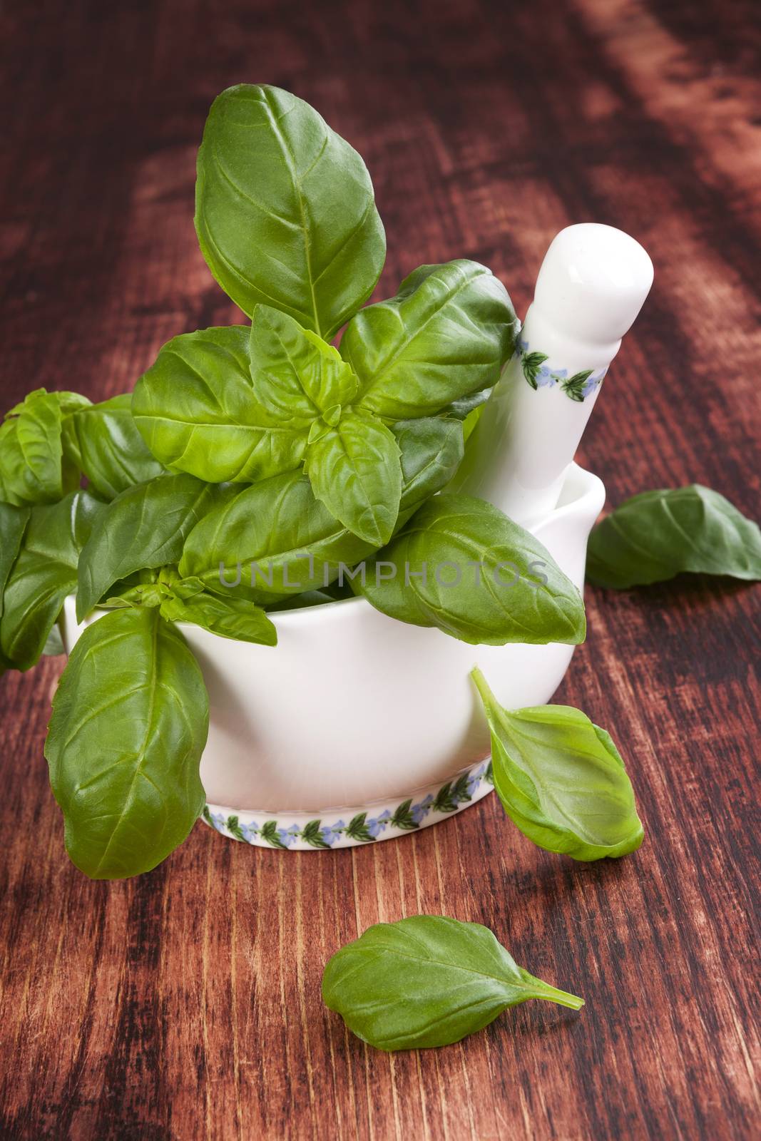 Basil. Culinary herbs. Fresh basil bunch in mortar with pestle on brown wooden background. Traditional cooking, rustic style.