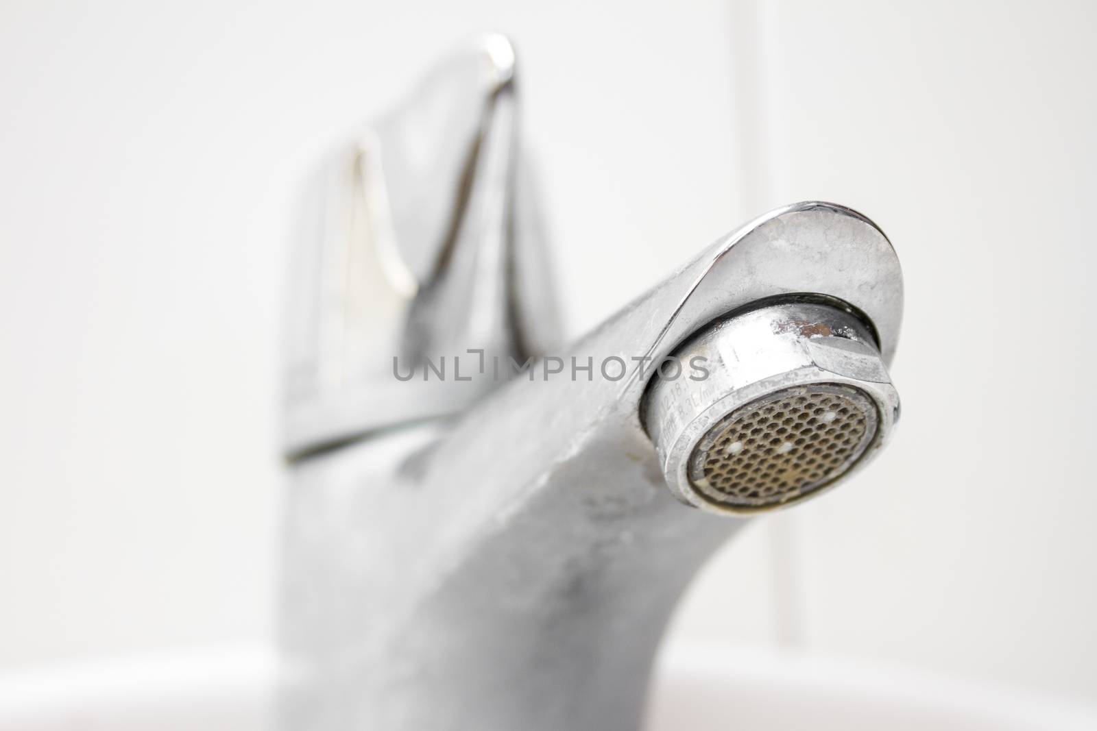 Modern style dirty faucet closeup view on white tiles background, small depth of field
