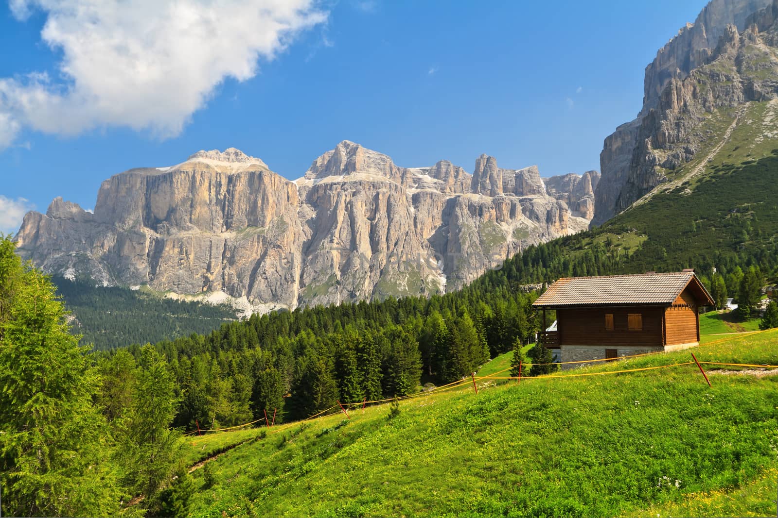 summer landscape in Fassa Valley with a small chalet beneath Dolomites mountains, Trentino, Italy