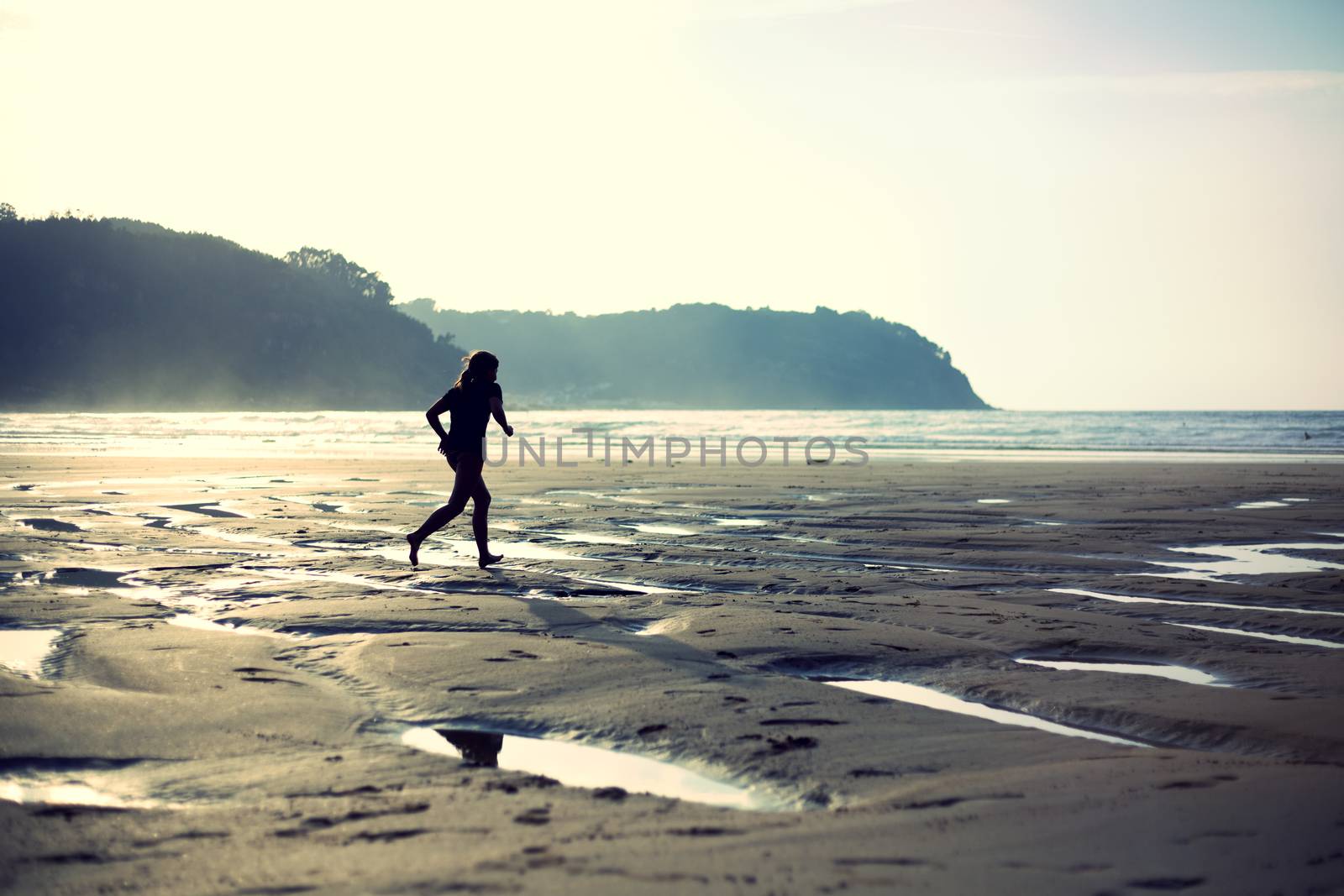 Backlight of a litlle girl running on the beach. Cross processing effect.