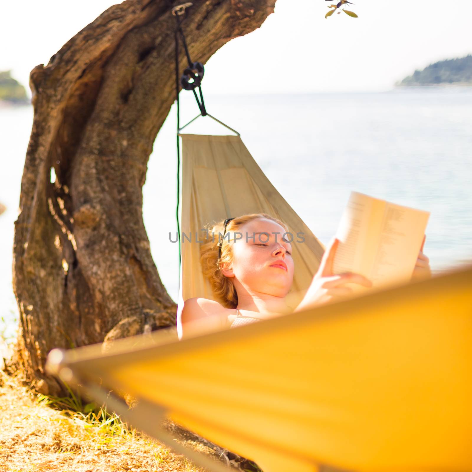 Beautiful girl lies on hammock on the beach reading book.