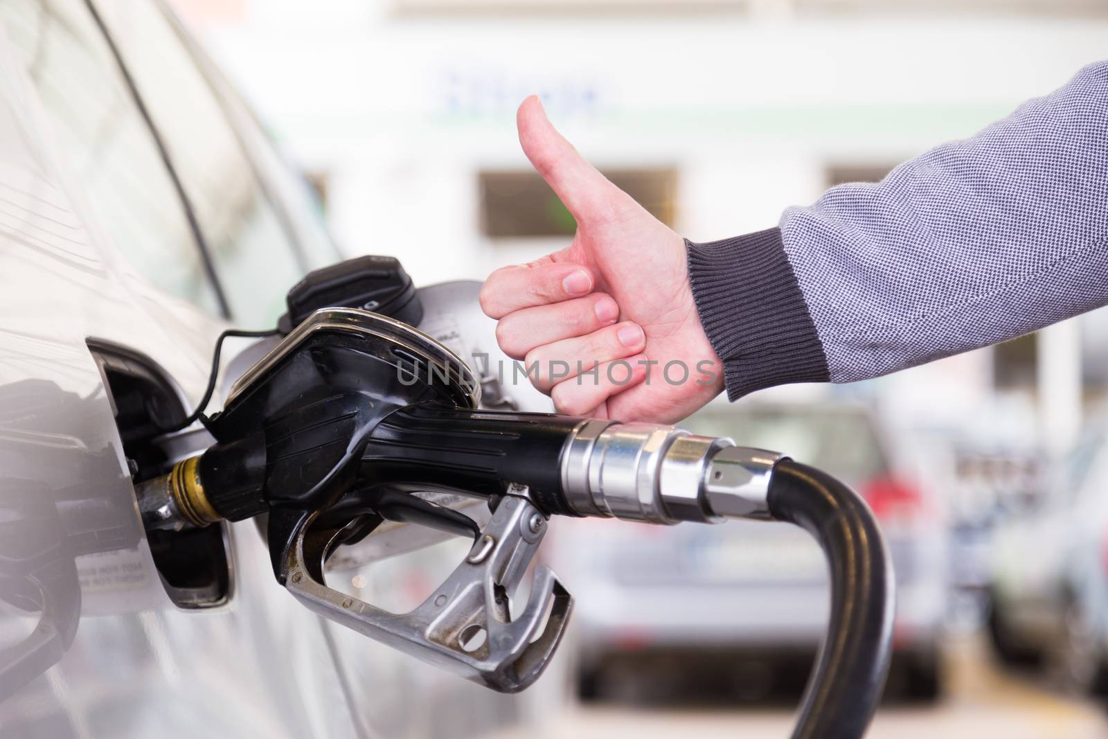 Petrol or gasoline being pumped into a motor vehicle car. Closeup of man, showing thumb up gesture, pumping gasoline fuel in car at gas station.