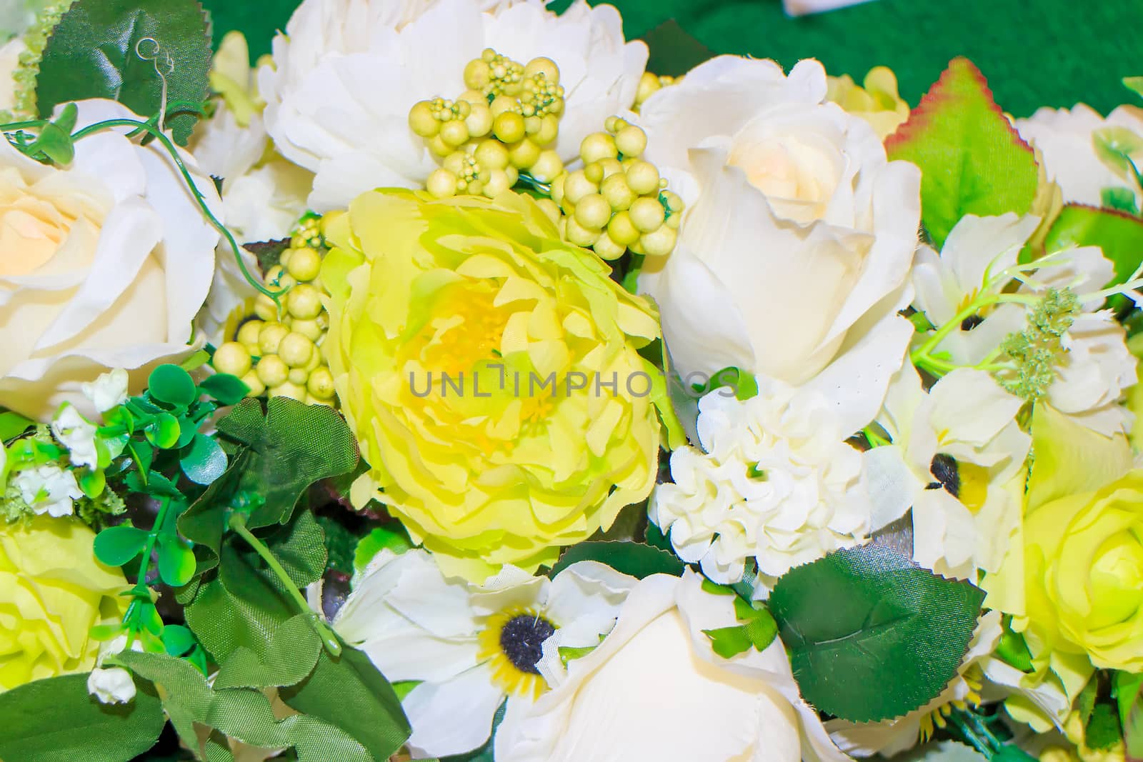 Whit and yellow fake flowers is on green leaves for background.