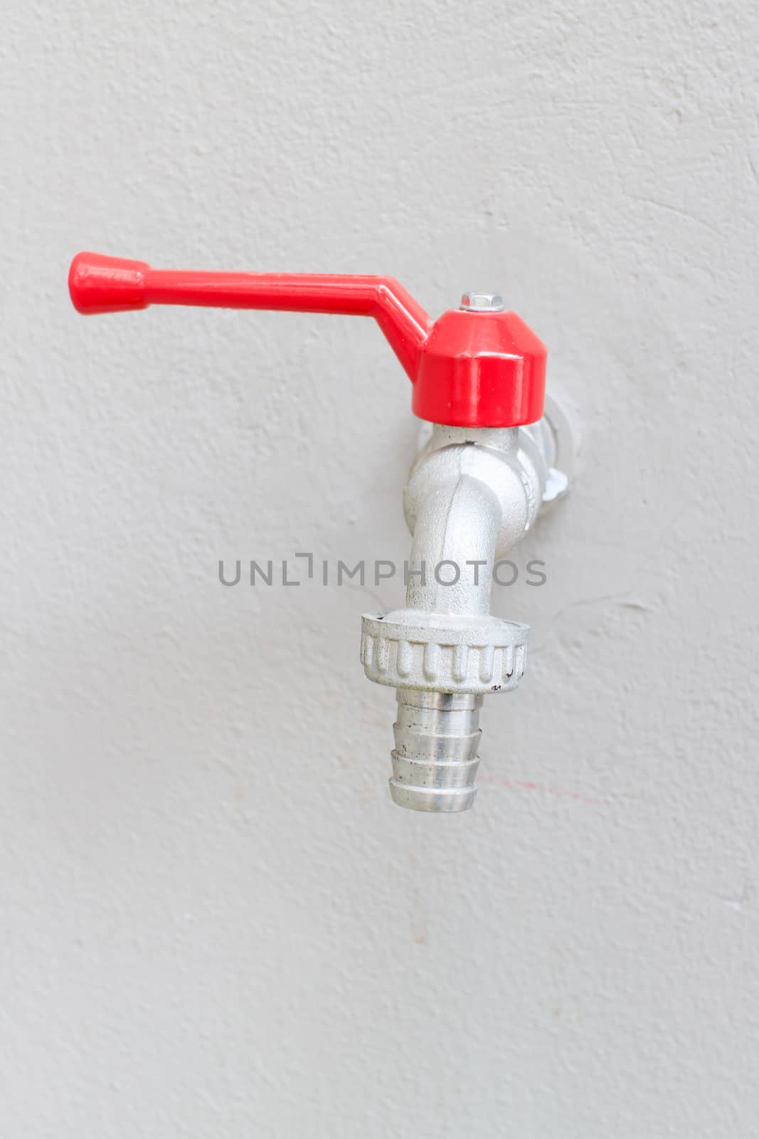 The silver and red faucet on white wall.