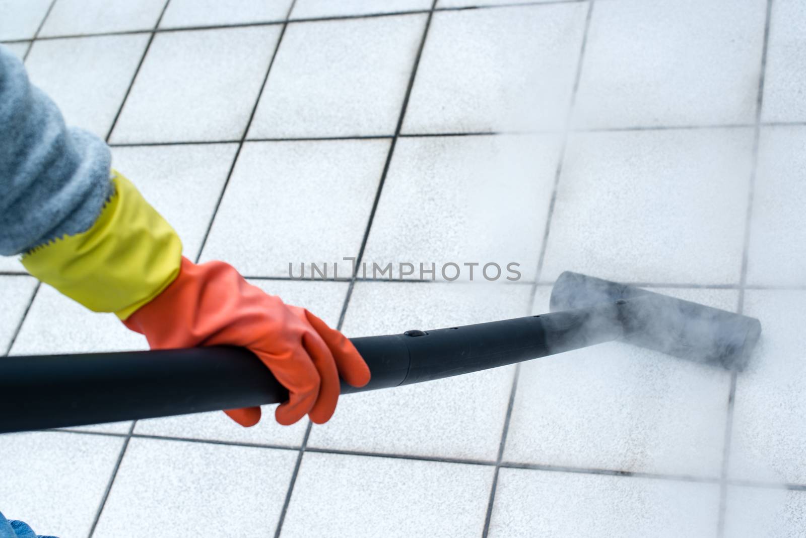 Woman wearing rubber gloves using steam cleaner to brighten up balcony tiles