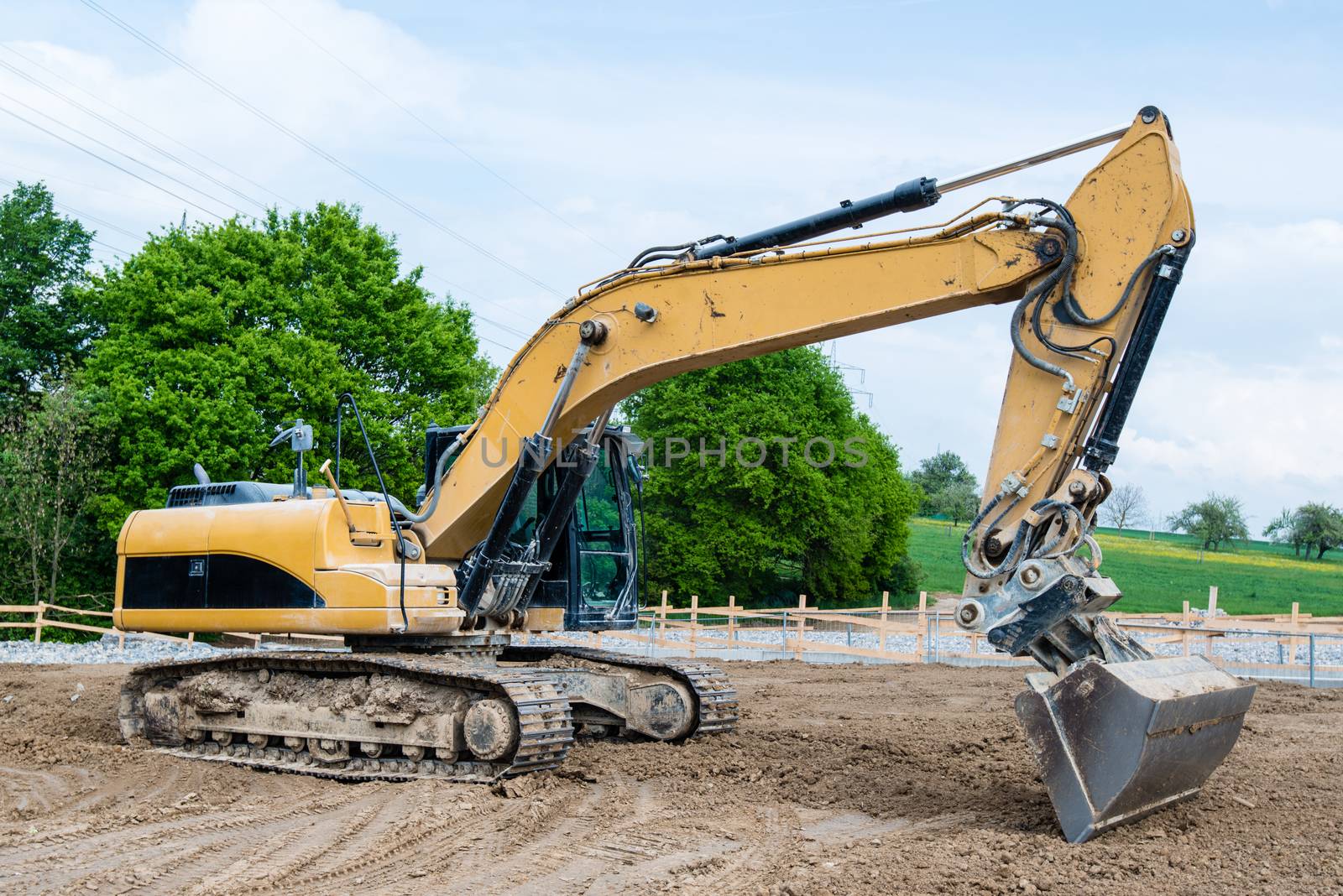 Big excavator parked on construction site with trees and cloudy blue sky in the background