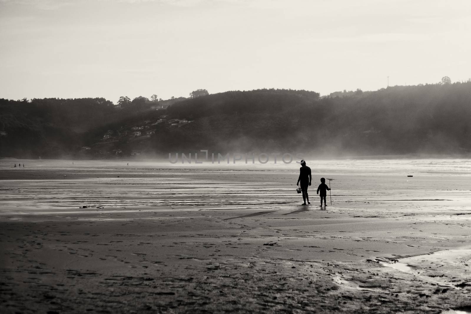 Mother and son on the beach walking and looking for shells. Sunset in backlight.