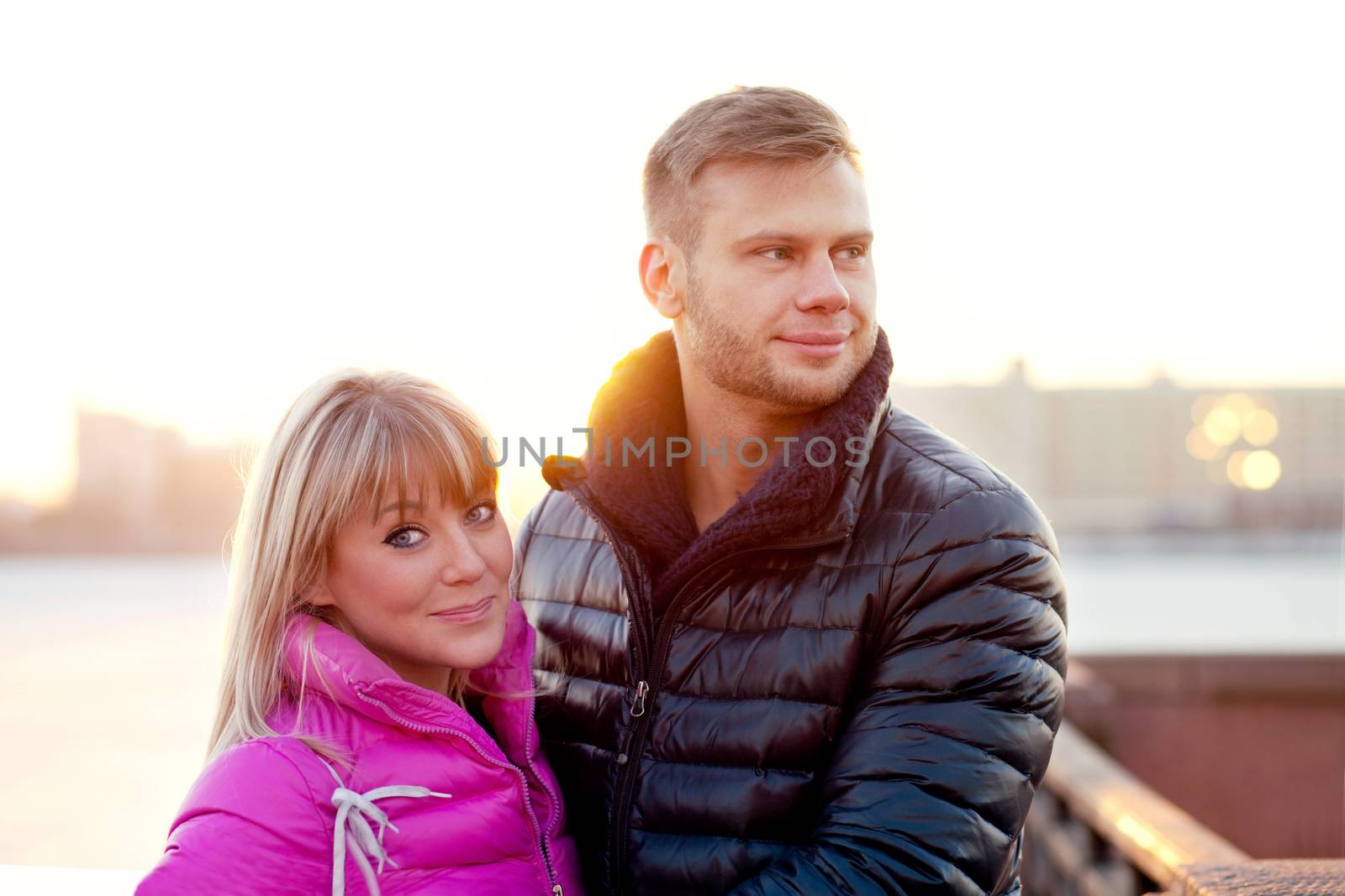 Young couple in winter cold clothes smiling in the sunset sun