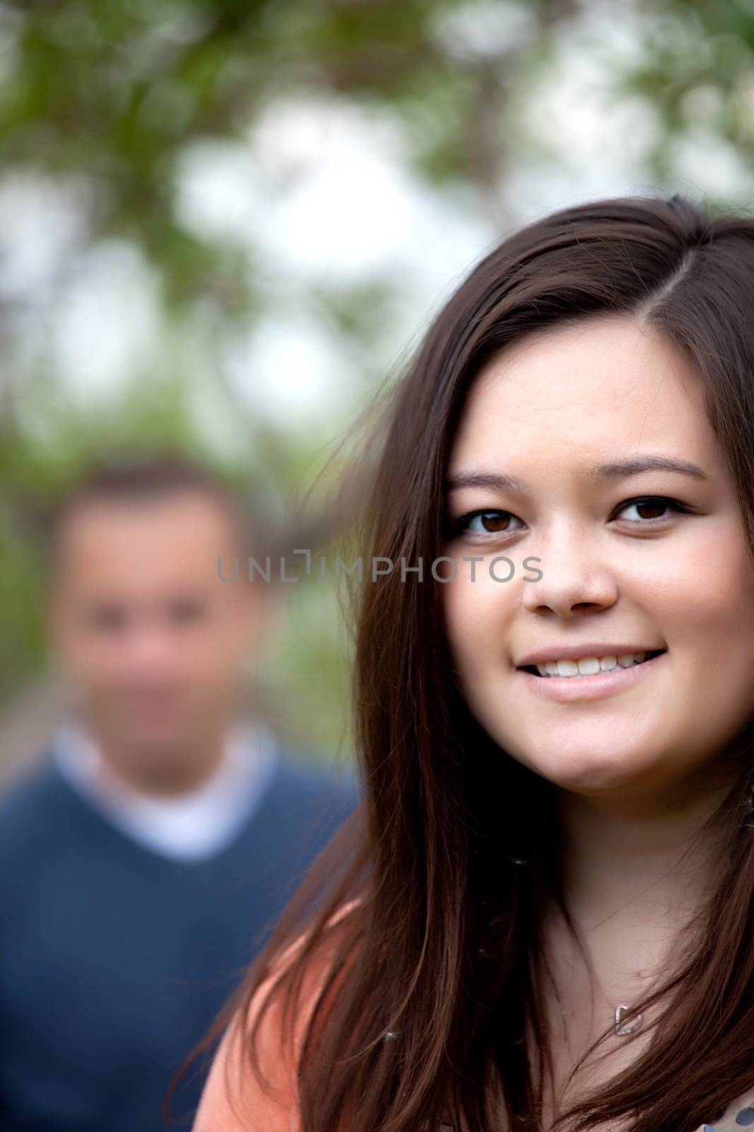 Young happy couple with the woman in the foreground and her partner in the background.  Shallow depth of field.