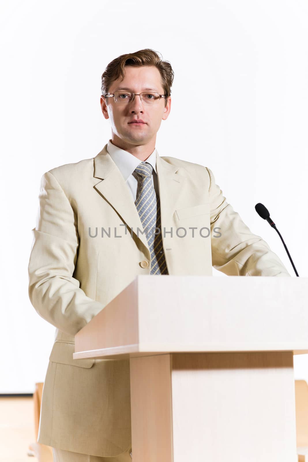 male speaker stands behind a podium on the stage and looking into the hall