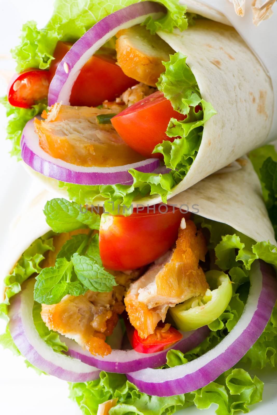 Chicken tortilla with fresh healthy salad ingredients including lettuce, onion, tomato and herb, close up view of two on top of each others