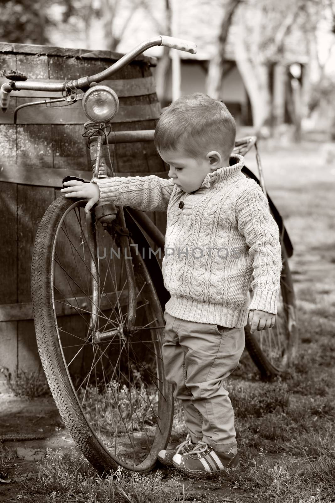 2 years old curious Baby boy walking around the old bike on sepia brown color