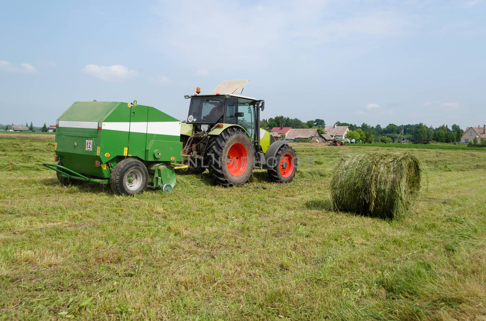 tractor bailer collect hay in field. Agricultural machine making hay bales. Seasonal rural works.