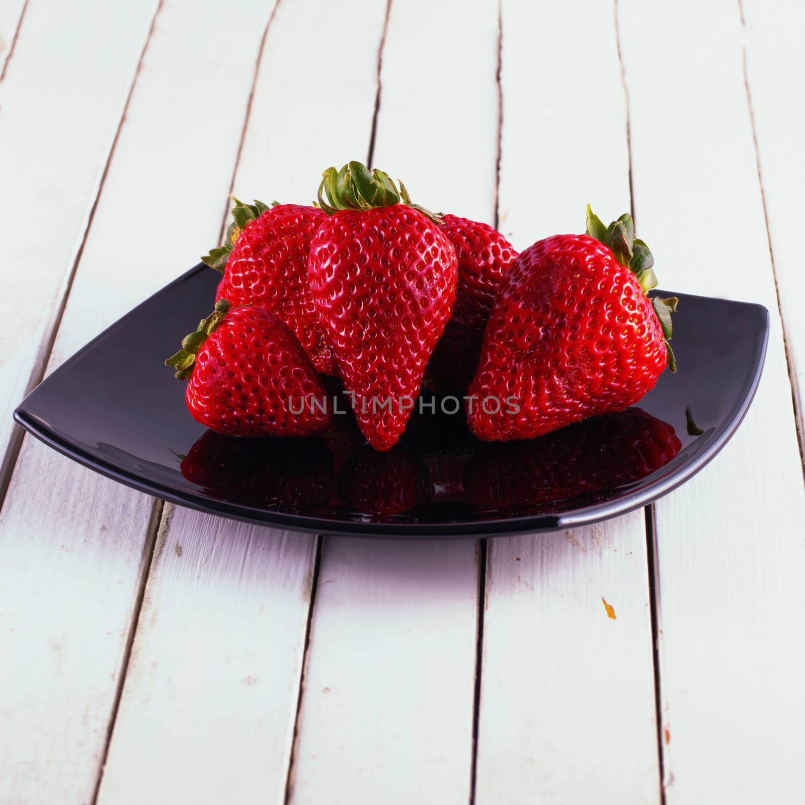 Strawberries over a black plate, over white wood