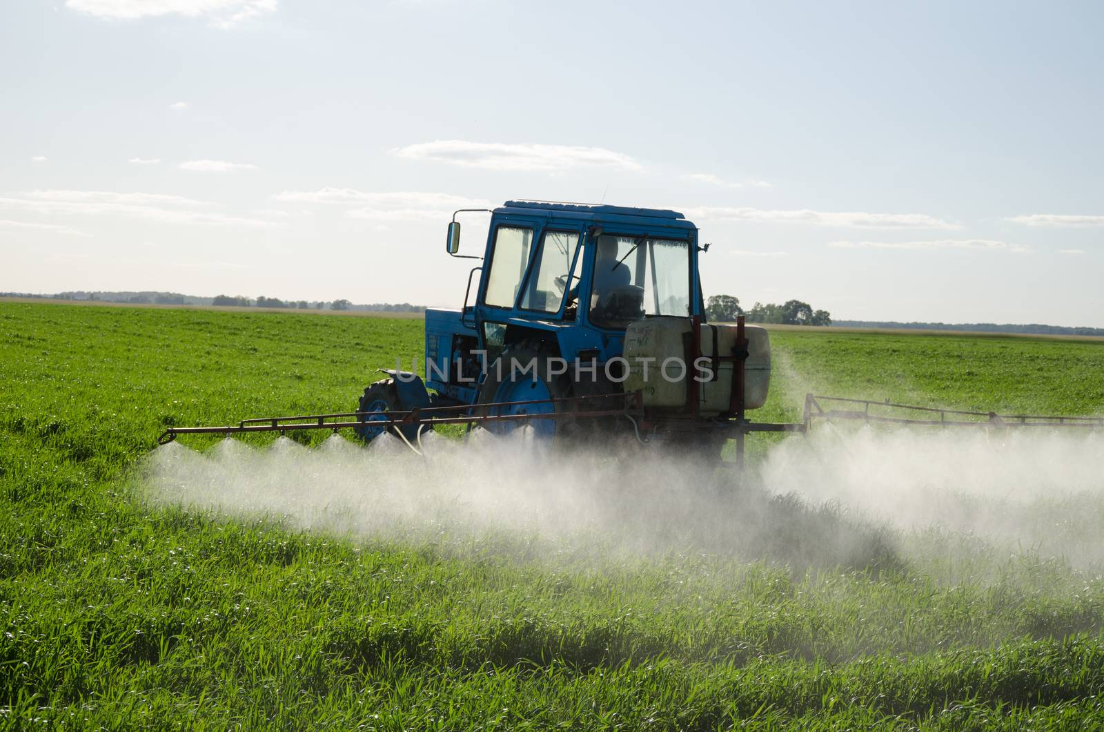 Tractor spray fertilize field with insecticide herbicide chemicals in agriculture field and evening sunlight.