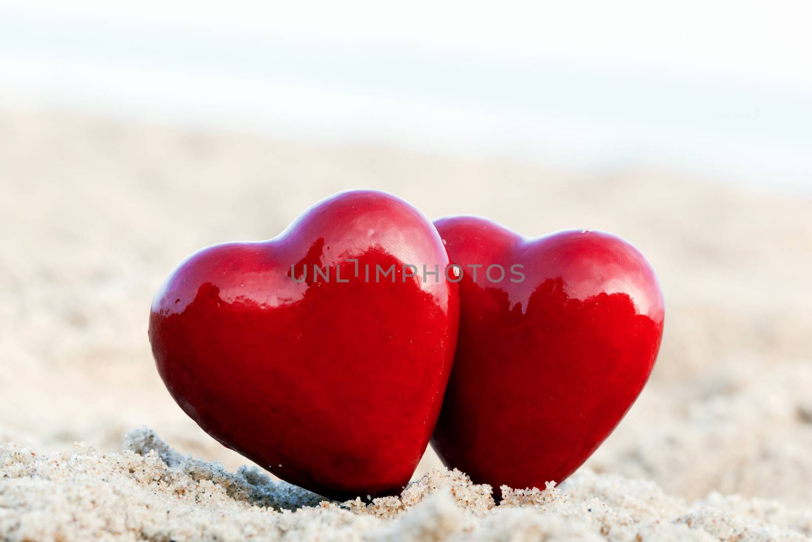 Two red hearts on the beach symbolizing love, Valentine's Day, romantic couple. Calm ocean in the background
