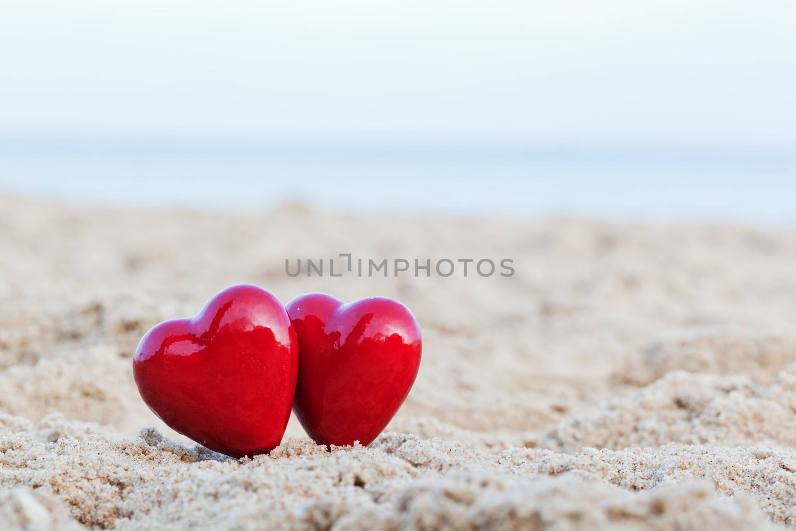 Two red hearts on the beach symbolizing love, Valentine's Day, romantic couple. Calm ocean in the background