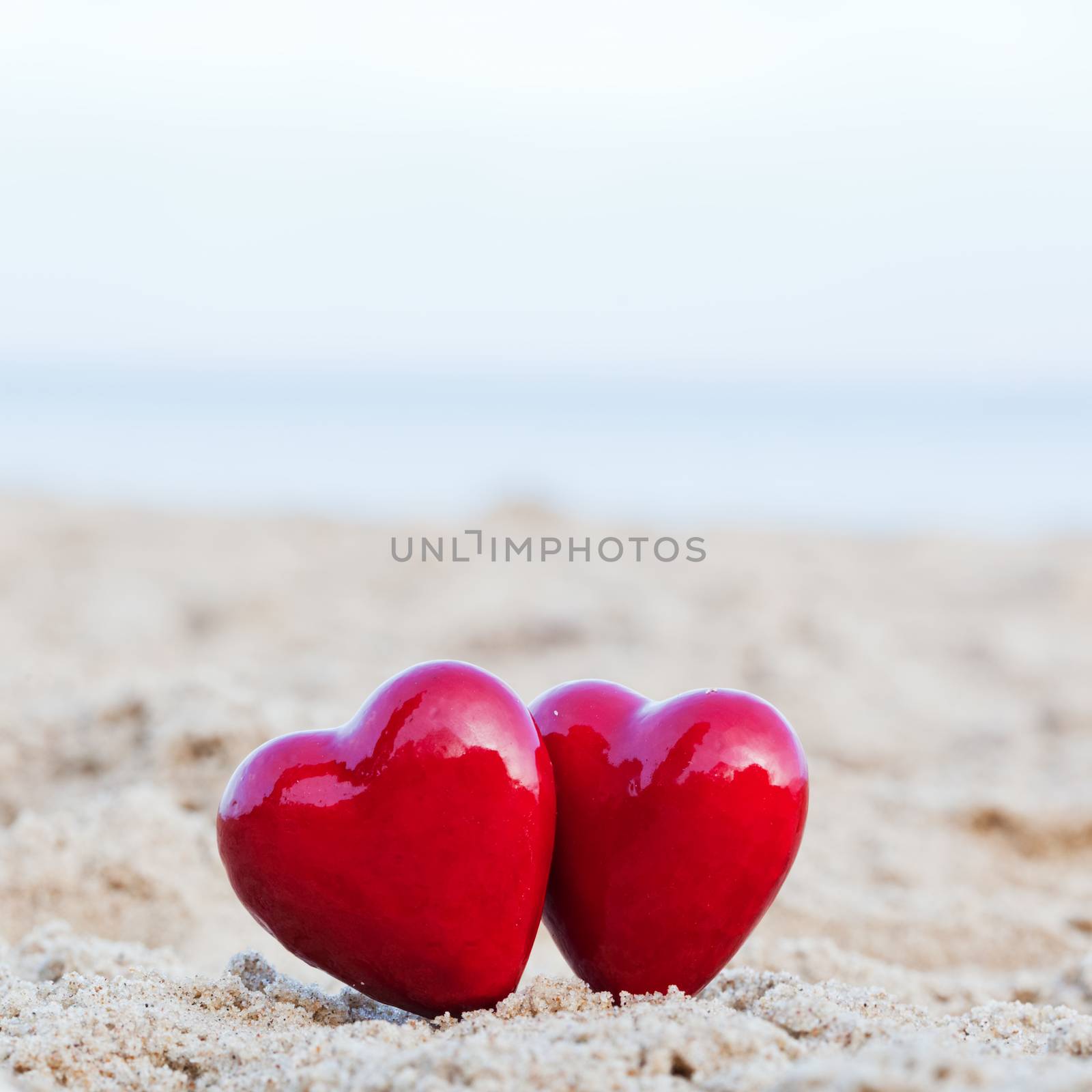 Two red hearts on the beach symbolizing love, Valentine's Day, romantic couple. Calm ocean in the background