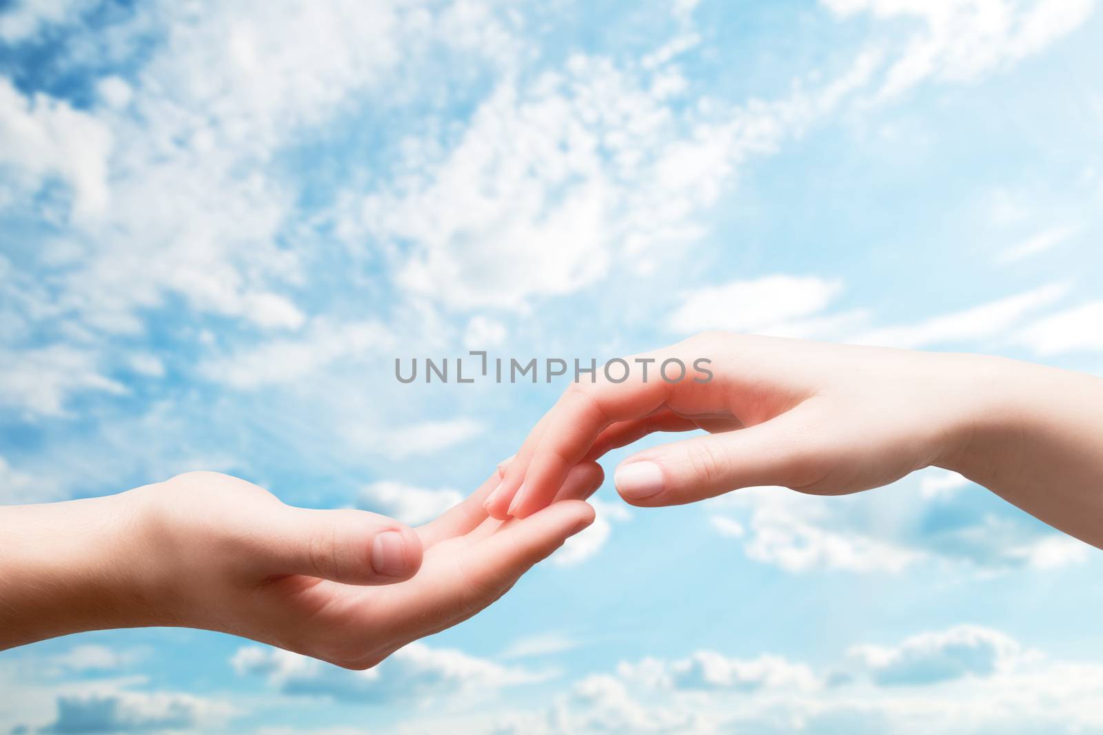 Man and woman hands touch in gentle, soft way on blue sunny sky. Concepts of connection, hope, faith, help, love.